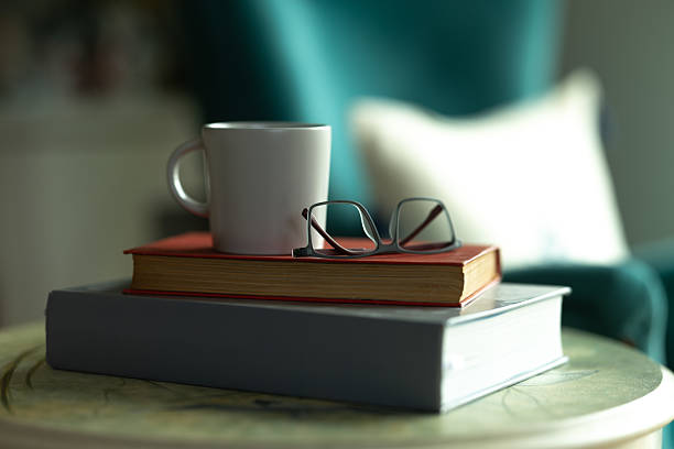 istock Books, reading glasses, and a coffee mug sit on a small table next to a comfortable chair, suggesting a cozy afternoon of reading 2207844507