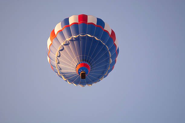 A red white and blue hot air balloon with other hot air balloons in the background.