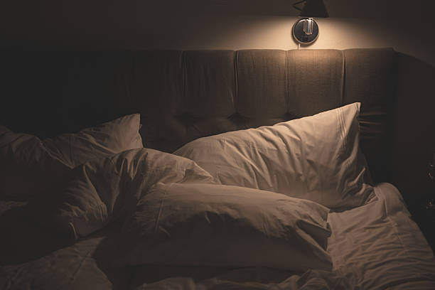 istock dimly lit bedroom with dark upholstered headboard and white bedding.. 2207846626