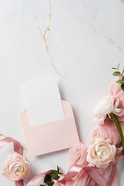 istock Romantic flat lay witn pink envelope, blank card, roses, greenery, and a ribbon on marble. Ideal for wedding invitations, event announcements, or feminine branding 2207849146