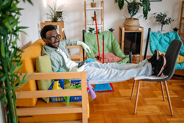 istock Young man cleaning his apartment and taking a break and resting using mobile phone while sitting on sofa close to cleaning equipment 2207850113