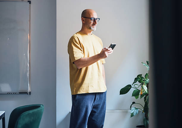 istock Casual Man Standing Indoors Using Smartphone Near Plants and Whiteboard 2207850513