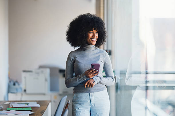 istock Confident Businesswoman Smiling While Holding Smartphone in a Bright Office 2207850519