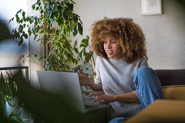 istock A smiling young woman sits on a comfortable sofa, sipping coffee while working on her online job on a laptop. 2207855083