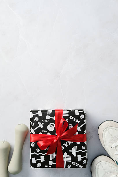 istock Fitness gift box with red ribbon, sneakers, and dumbbells on marble table. 2207855517