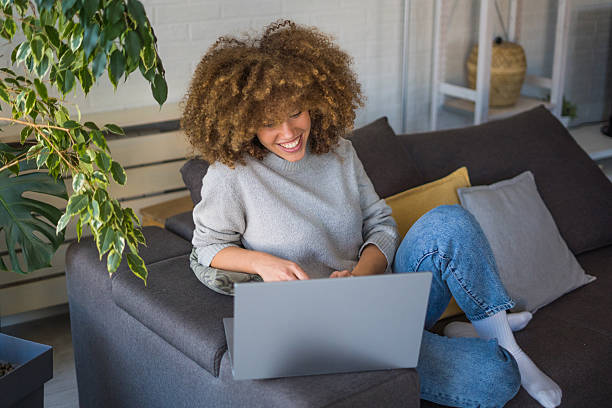 istock A young woman with natural curls sits on a comfortable sofa, enjoying her coffee while using her laptop. 2207855758