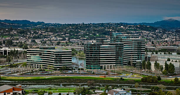 Drone shot orbiting a set of office towers with hills covered in houses in the background at dawn in Redwood City, California. Redwood City is a suburb in San Mateo County on the San Francisco Peninsula, and considered part of Silicon Valley. This area, known as Redwood Shores, is built on reclaimed land in the marshes of San Francisco Bay and is home to many big tech companies.\n\nAuthorization was obtained from the FAA for this operation in restricted airspace.