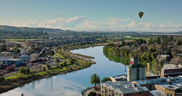 Aerial shot of a hot air balloon flying over the the river in the town of Napa in Northern California wine country on a sunny day in springtime. \n\nAuthorization was obtained from the FAA for this operation in restricted airspace.