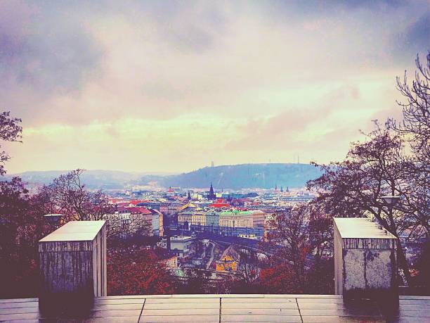 Stunning panoramic autumn view of Prague cityscape featuring Vltava River, historic stone bridges, and colorful fall foliage. Czech Republic capital showcases baroque church with distinctive green copper dome, medieval bell towers, and Petrin observation tower on hillside covered with golden orange autumn trees. Picturesque European travel destination captures architectural heritage, river waterfront, and vibrant seasonal colors. Perfect Prague landmark photography showing old town charm during peak fall season.