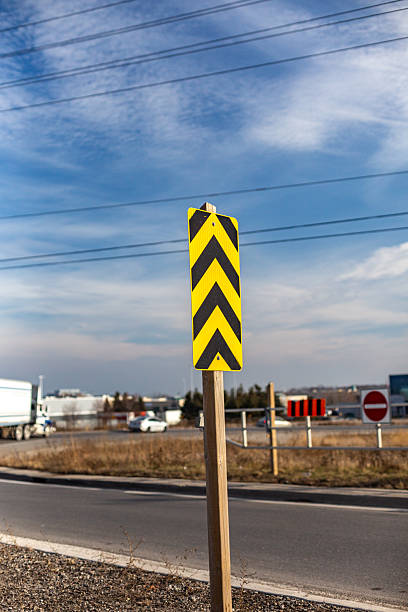 Diagonal Chevron Traffic Sign beside Road on a Sunny Day Yellow and black diagonal chevron road sign indicating directionality, located beside a roadway under a clear sky. road chevron warning signs stock pictures, royalty-free photos & images