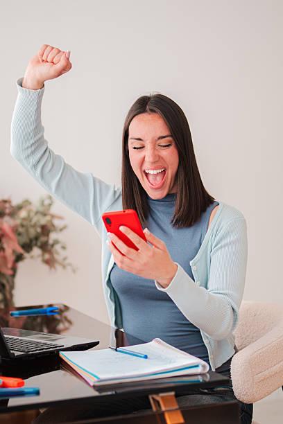 istock Excited young woman celebrating a significant win while using her smartphone, expressing pure joy and triumph with her energetic gestures and bright smile in a moment of happiness and success 2207862033