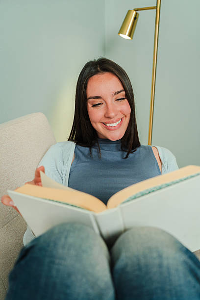 istock A joyful woman deeply engaged in reading a captivating book while sitting comfortably on a cozy sofa, radiating happiness and contentment with her smile and relaxed demeanor in a serene moment 2207866641