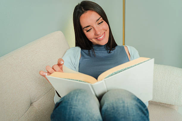 istock Enthusiastic woman enjoying a captivating book while sitting comfortably on a cozy sofa, deeply engaged in reading and smiling with joy and satisfaction that comes from a good story 2207867064