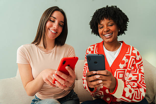 istock Two cheerful women happily using their smartphones while sitting on a couch, enjoying a delightful moment together as they interact and share experiences through their mobile applications and engaging content 2207869318