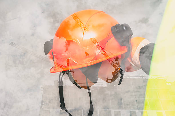 Double exposure image with orange helmet against construction site with crane and building. Industrial development and safety concept