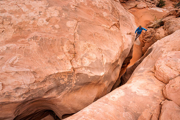 Tight Squeeze Hiking in Slot Canyon - Beautiful red rock canyon with narrow slot drop into canyon wash. Man exploring climbing through slot canyon in smooth red sanstone rock in a desert canyon environment.