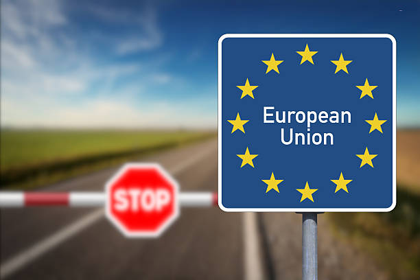 A blue European Union sign stands beside a road with a blurred stop barrier in the background.