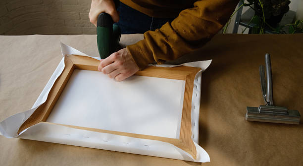 istock Artist's hands stretching canvas on stretcher bars using staple gun 2207891358