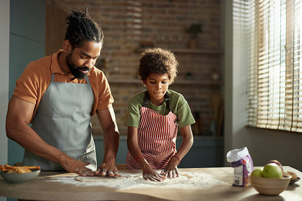 Black father and son making pizza dough in the kitchen.