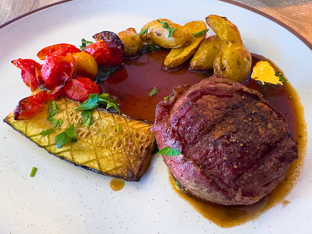 istock A beautifully plated dish features a seared beef medallion with roasted potatoes, tomatoes, and zucchini, drizzled with a rich sauce 2207894436