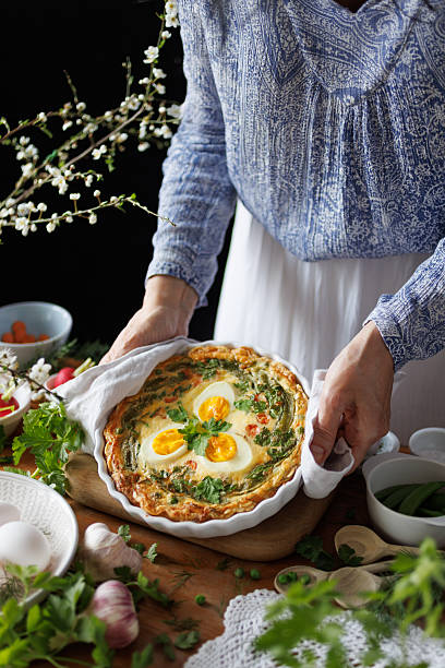 Woman holding casserole dish with quiche with boiled eggs and vegetables, close-up. Easter food concept
