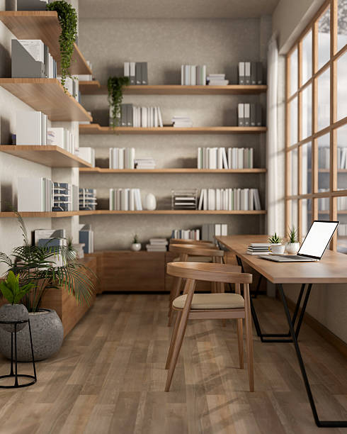 White screen laptop on long table next to glass wall and large bookshelf. Cosy library or study room