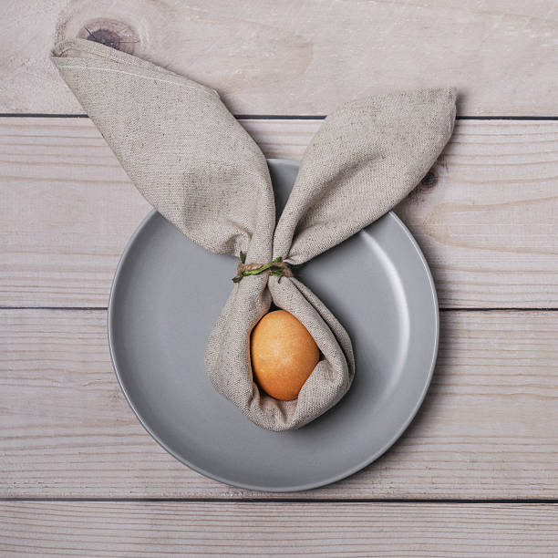 On the table there is a gray plate and a painted egg decorated with a bunny shaped napkin. Christian Easter tradition. Flat lay.