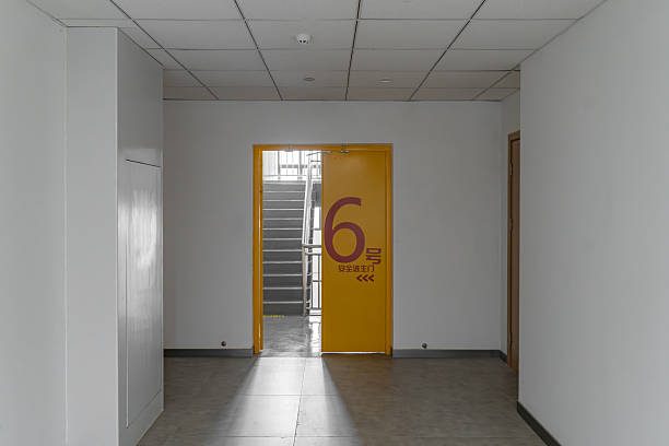 Lit Entrance Framing Empty Stairwell And Banister, Institutional Corridor Beyond Glass Door, Neutral Tiles, Posted Notice On Door, Quiet