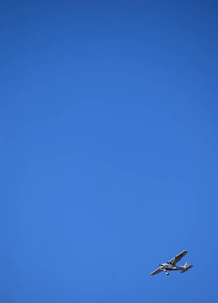 The photograph is dominated by a vast expanse of clear, blue sky, creating a sense of openness and tranquility. In the lower right corner, a white monoplane appears slightly tilted, adding a dynamic element to the composition