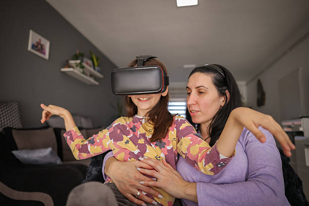 A cozy family moment as a little girl plays a VR game, embraced by her mother, who watches her with love and encouragement.
