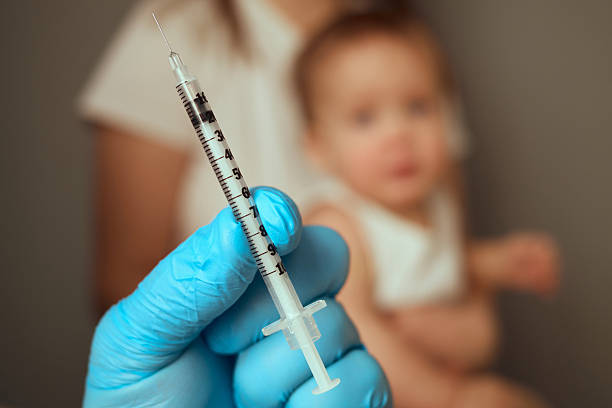 istock A parent holds a syringe ready for vaccination, focusing on the inoculation process. A child sits nearby, demonstrating a common healthcare practice and the importance of immunization 2207905422