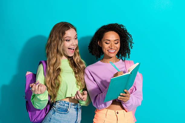 istock Two young female students smiling and sharing notes against vivid turquoise background 2207905915