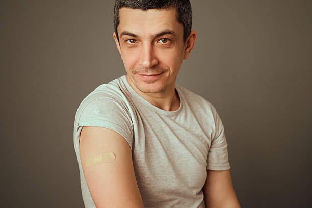 istock A man sits confidently, revealing his arm with a bandage after getting vaccinated. He appears relaxed, demonstrating the importance of health and wellness in a simple indoor environment 2207905930