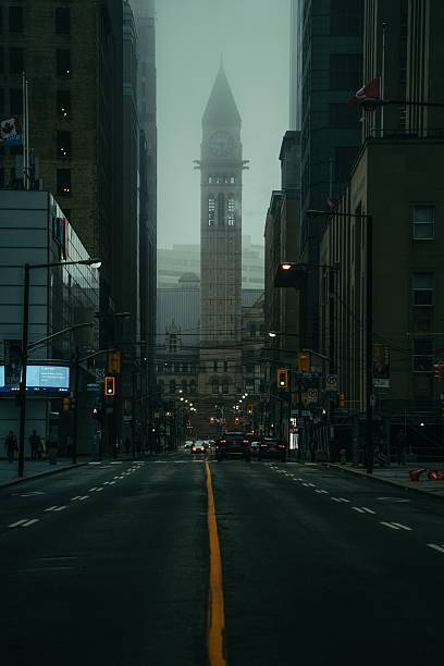 A moody urban scene featuring a clock tower in the misty morning light on a deserted street in Toronto, Canada.