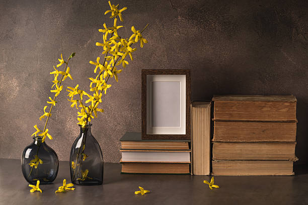 Minimalist still life composition featuring a wooden vase with two vibrant yellow sunflowers, placed next to two empty wooden picture frames—one light and one dark—against a clean white background. The combination of natural materials and neutral tones creates a warm, rustic, and artistic atmosphere. The image conveys themes of creativity, home decor, simplicity, and Scandinavian-inspired design.