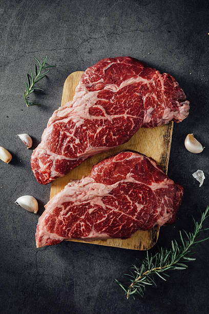 istock Fresh Raw Beef Steak on Wooden Board with Garlic and Herbs on Dark Background 2207911238