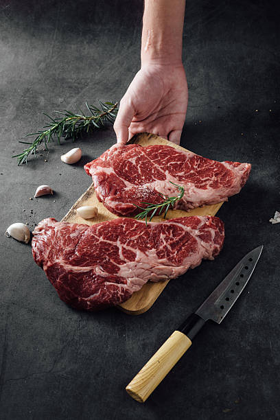 istock Raw Fresh Meat Cuts with Hand Holding on Wooden Board and Kitchen Knife on Dark Surface 2207911256