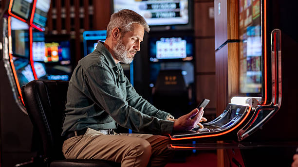 istock Serious Man Using Mobile Phone at Casino Slot Machine 2207911523
