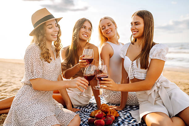 Happy girlfriends spending time together on a sunset beach. Four beautiful women with glasses in their hands having fun outdoors. Concept of friendship, fun. Lifestyle.