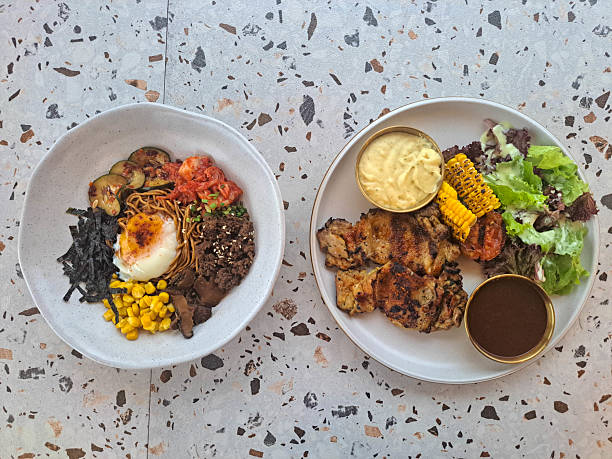 Fried Dry Ramen Noodle With Minced Beef, Onsen Egg, Shitake Mushroom, Corn, Nori, Kimchi, Pickled Cucumber And Spring Onion. Herb Grilled Chicken Steak With Chicken Leg, Grilled Corn, Grilled Potato, Mesclun. Food Menu. Top View.