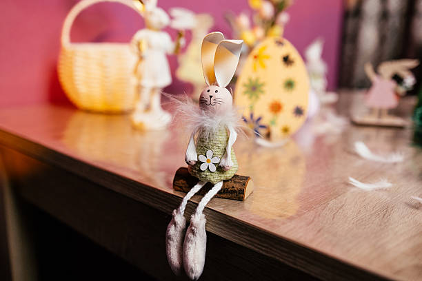 istock A whimsical bunny figurine sits on a wooden surface, surrounded by various vibrant Easter decorations, such as eggs and baskets, creating a festive atmosphere. 2207913420