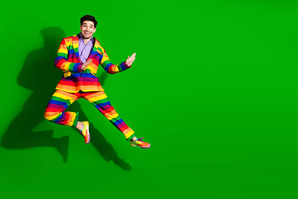 istock Young man in a vibrant rainbow-striped suit jumping joyfully against a bright green background, expressing fun 2207914363
