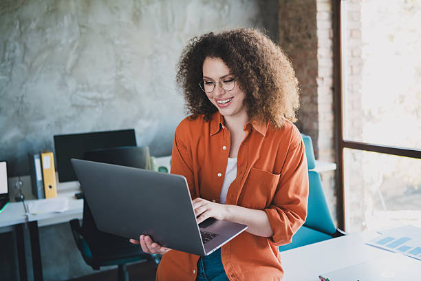 istock Smiling Young Professional with Curly Hair Working on Laptop in a Modern Daylight Office Interior 2207918982