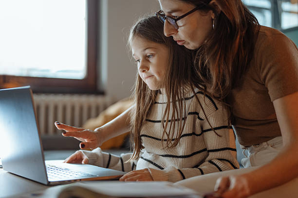 istock Mother and daughter talking at home while looking at a school book and using a laptop in a comfortable living room 2207919171