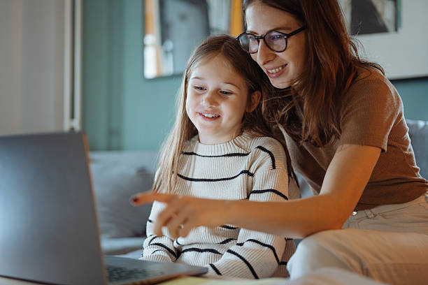 istock Mother and daughter talking at home while looking at a school book and using a laptop in a comfortable living room 2207919183