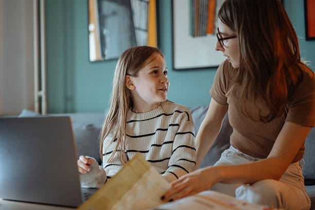 istock Mother and daughter talking at home while looking at a school book and using a laptop in a comfortable living room 2207919184