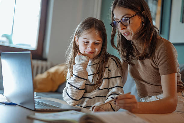 istock Mother and daughter talking at home while looking at a school book and using a laptop in a comfortable living room 2207919238