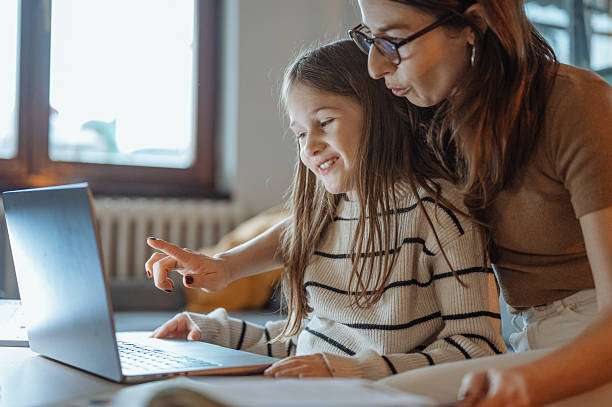 istock Mother and daughter talking at home while looking at a school book and using a laptop in a comfortable living room 2207919286