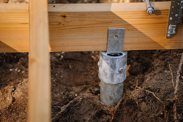 Close-up of a galvanized screw pile foundation supporting a wooden beam structure in sandy soil, showing detailed construction elements.