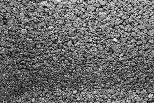 Close-up texture of asphalt or gravel surface. The image shows a uniform pattern of small, compacted stones creating a rough, granular texture in grayscale tones.